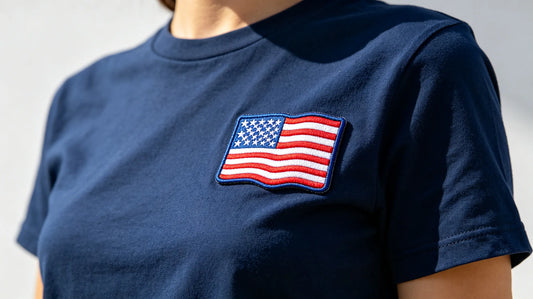 Close‑up of Fourth of July patriotic custom 3D embroidered patch sewn onto navy cotton T‑shirt, bright summer outdoor lighting