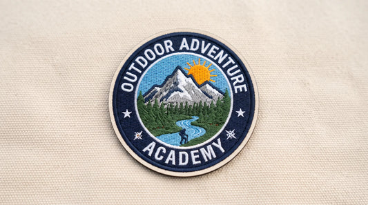 A complete, centered, circular embroidered hat patch for an outdoor academy, featuring a mountain logo.