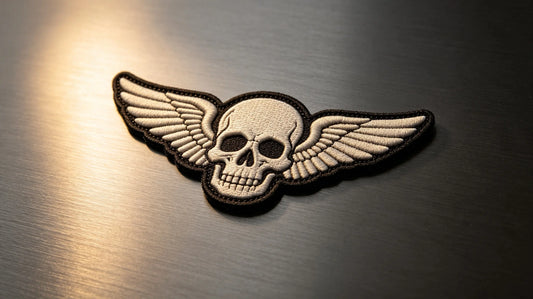 Single motorcycle club 3D raised foam embroidered patch, sculpted winged skull graphic, dark brushed metal background.