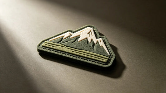 Single outdoor camping 3D raised foam embroidered patch, sculpted mountain graphic, matte dark taupe studio background.